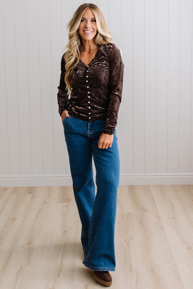BLONDE WOMAN IN DARK JEANS WEARING A ROMANTIC VELVET BURNOUT TOP WITH FEATURES LIKE, BURNOUT VELVET MESH FABRICATION, SCALLOPED LACE EDGE ACCENTS, FUNCTIONAL BUTTONS AND LONG SLEEVES