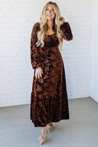 Woman wearing a brown floral dress against a white brick wall.