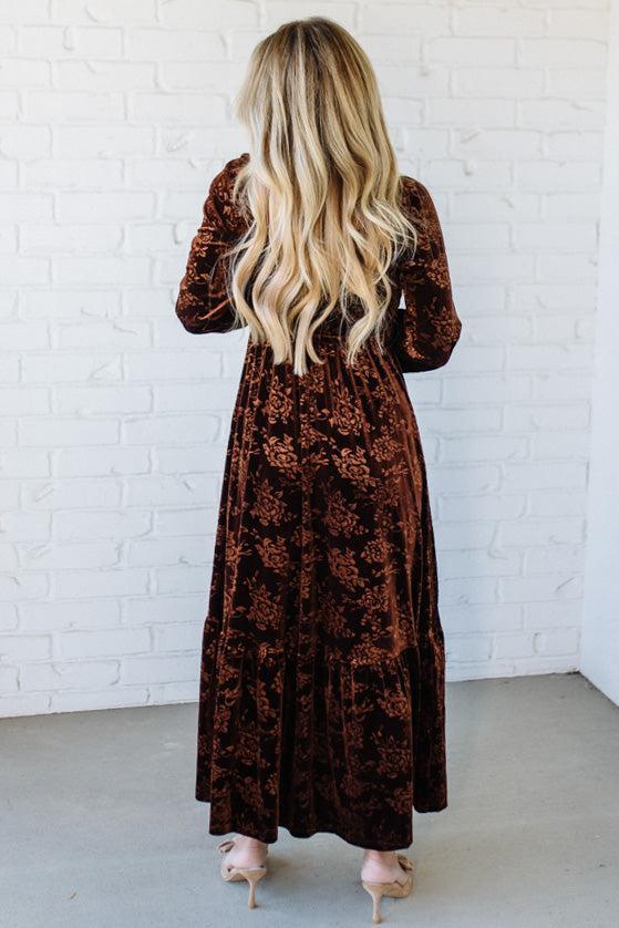 Person wearing a brown floral dress against a white brick wall.