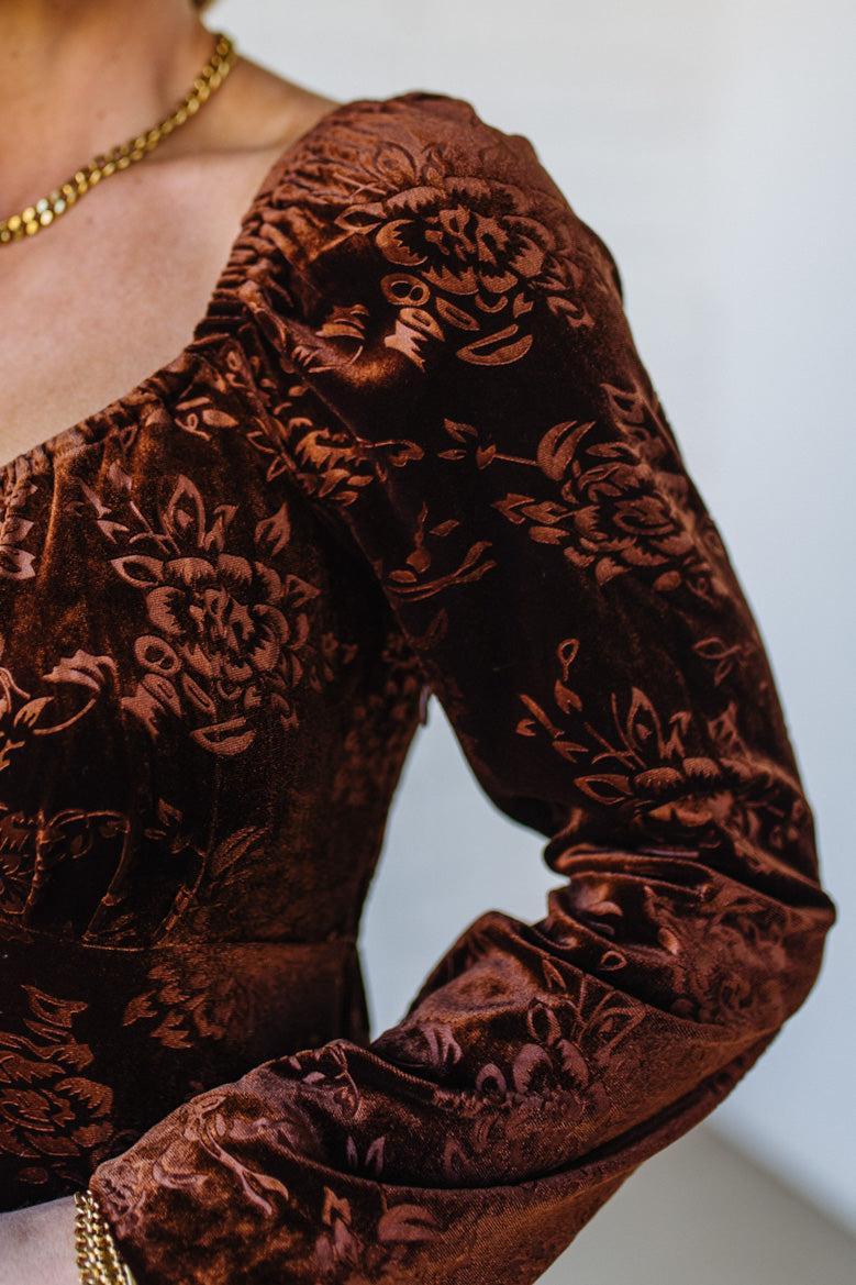 Brown floral velvet garment with long sleeves on a neutral background
