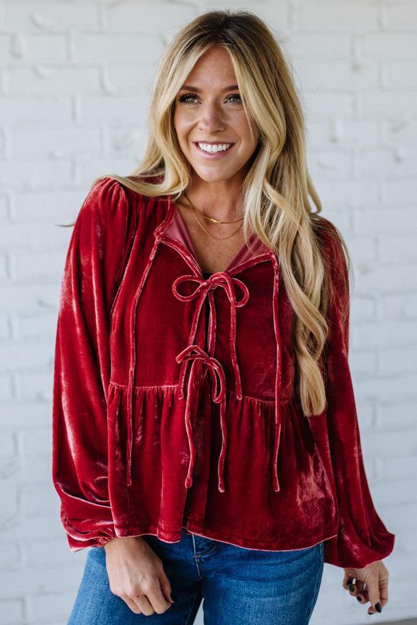 Woman wearing a red velvet blouse with a white brick wall background