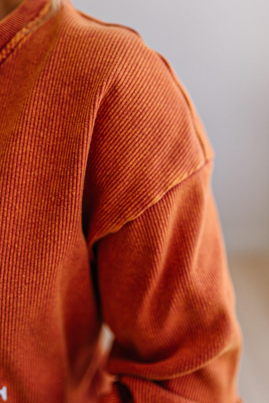 Close up of a blonde woman wearing a rust orange colored corduroy sweatshirt
