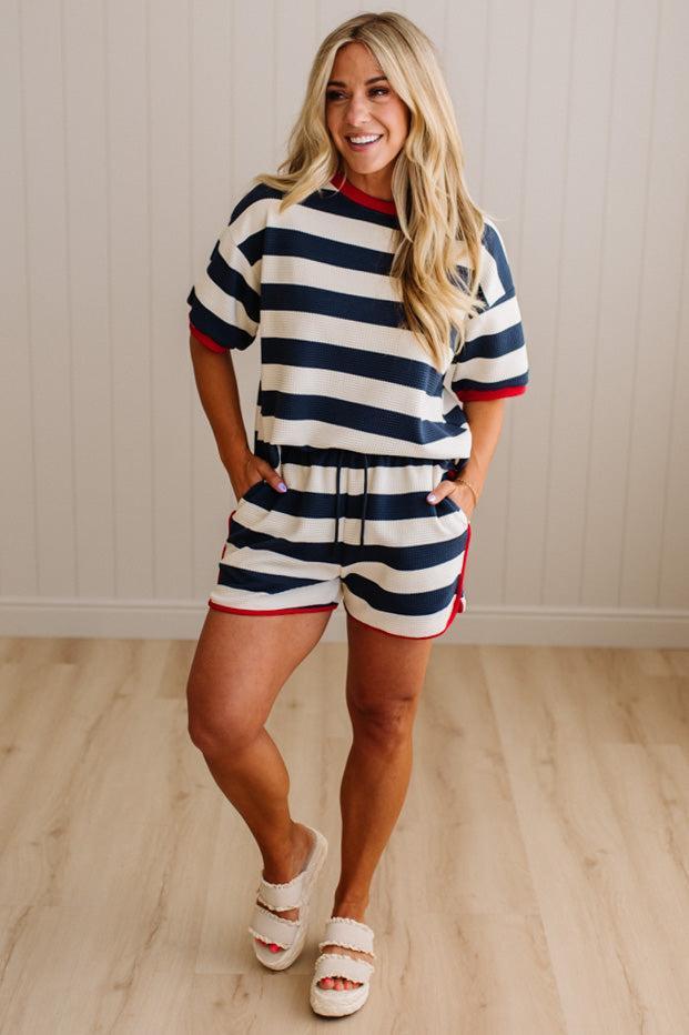 Woman wearing a striped outfit standing on a wooden floor with a neutral background