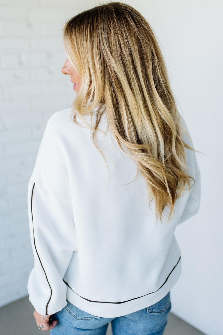 Person wearing a white sweater with black trim against a plain background