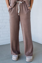 Brown ribbed pants with a white drawstring against a white brick wall.