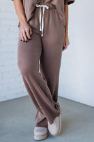 Person wearing a brown ribbed outfit with wide-leg pants and a matching top against a white brick wall.