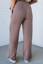 Person wearing brown ribbed pants against a white brick wall.