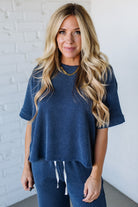 Woman wearing a blue ribbed top and matching pants against a white brick wall.