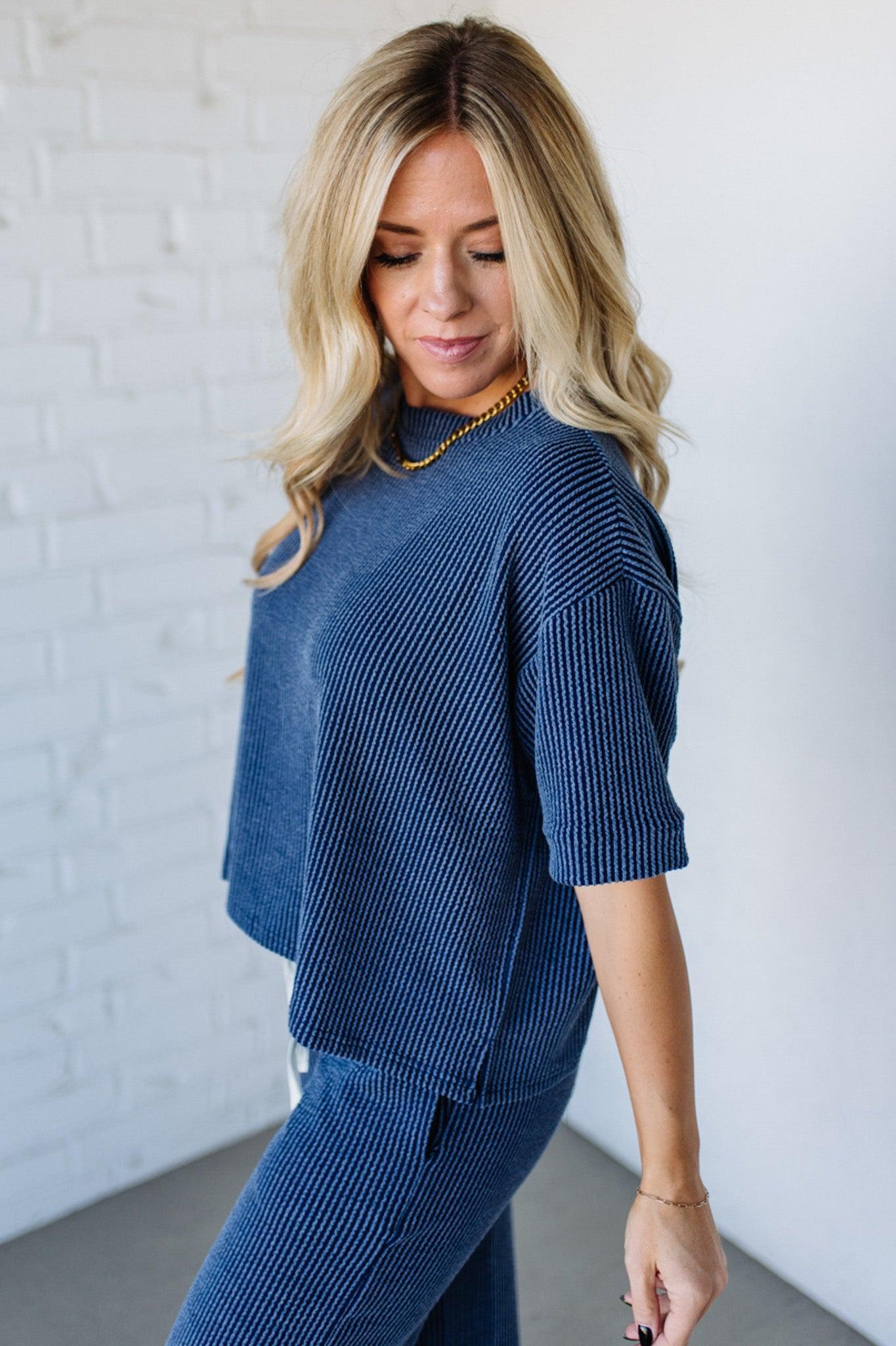 Woman wearing a blue textured outfit against a white brick wall.