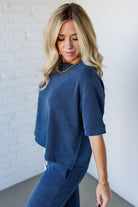 Woman wearing a blue textured outfit against a white brick wall.