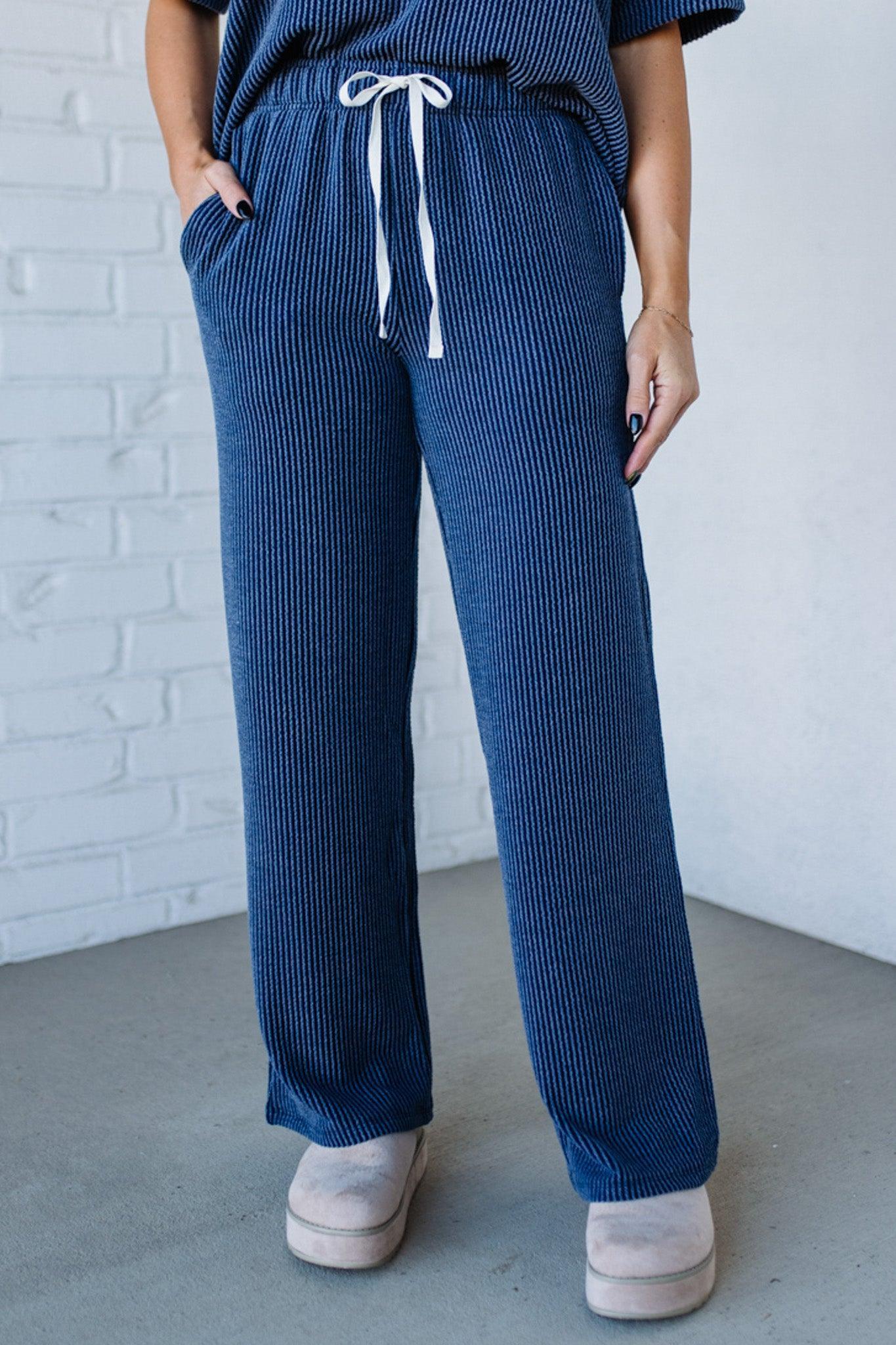 Person wearing blue ribbed pants with a white drawstring against a white brick wall.