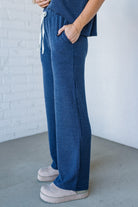 Person wearing blue ribbed pants with white sneakers against a white brick wall.