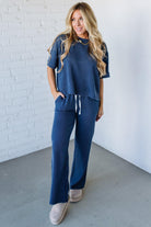 Woman wearing a blue waffle knit outfit against a white brick wall.