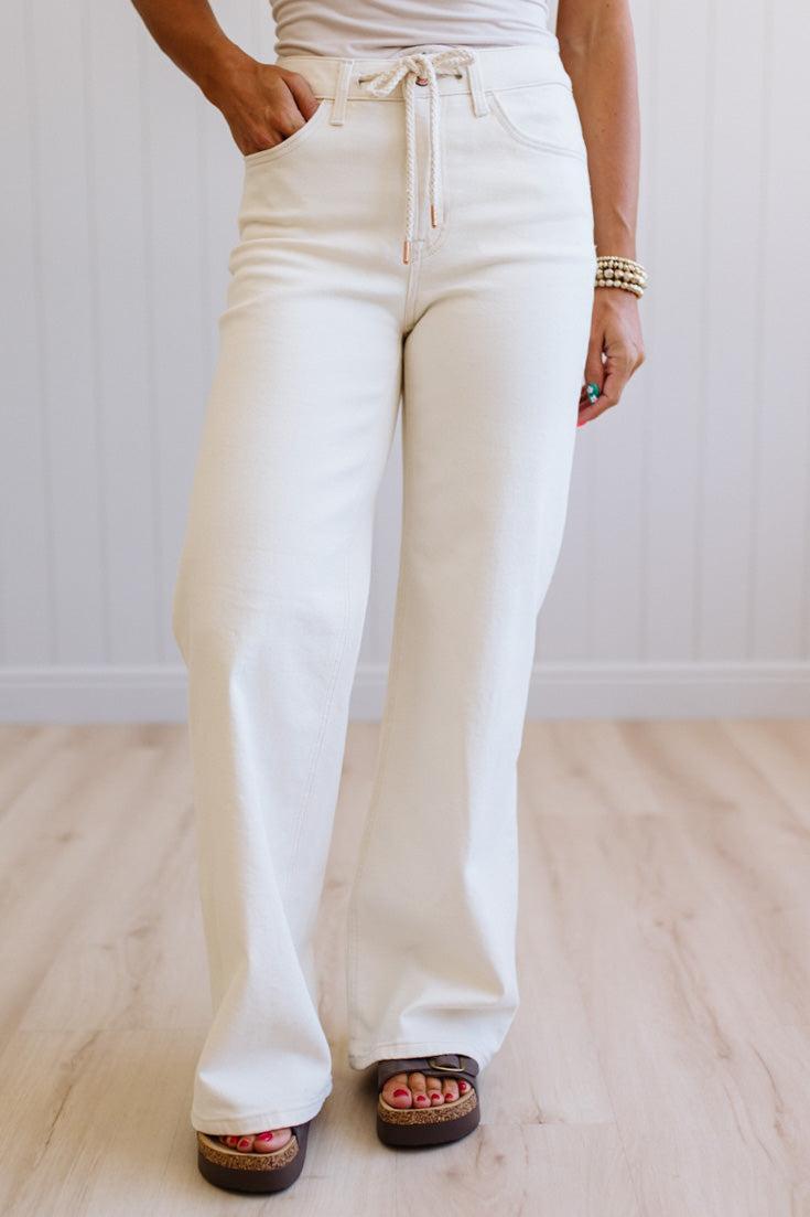 Person wearing white flared pants with a neutral background