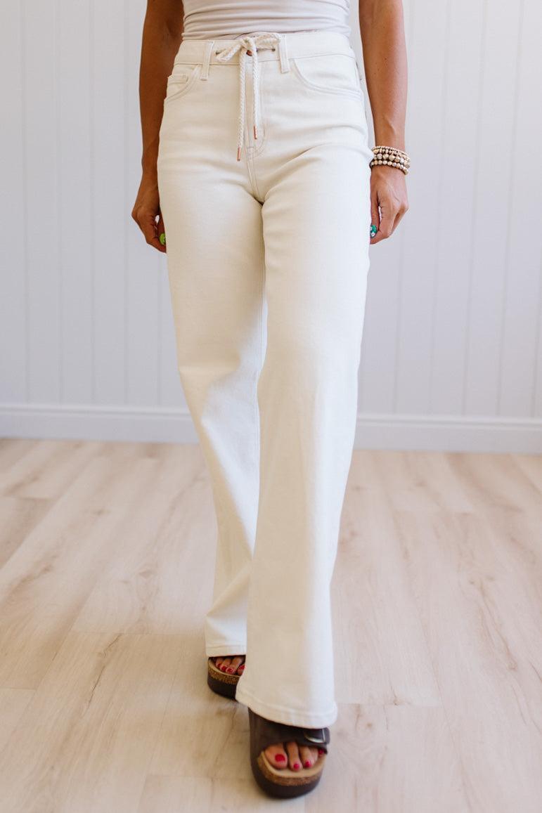 Person wearing white pants on a light wooden floor with a white wall background