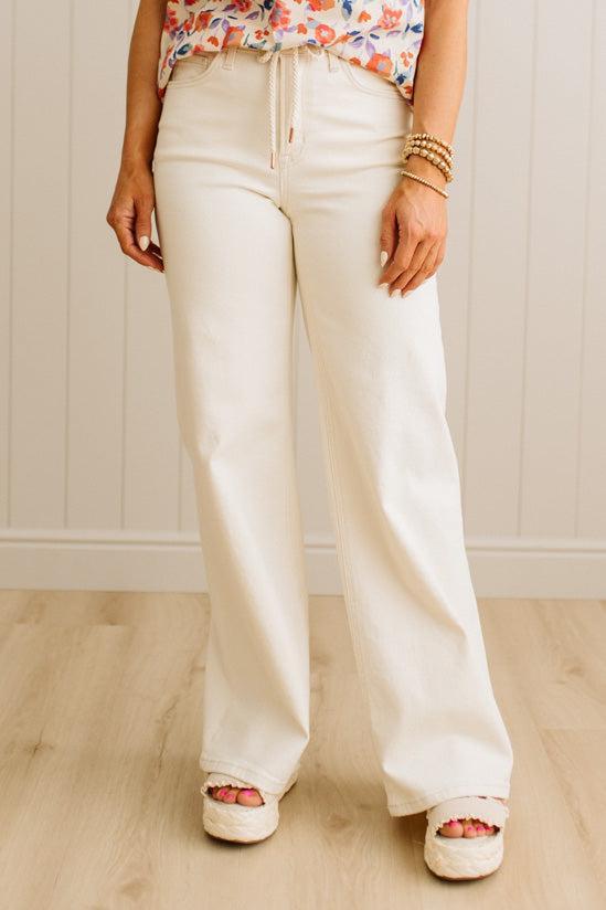 Person wearing white wide-leg pants with a colorful top against a light wooden panel background