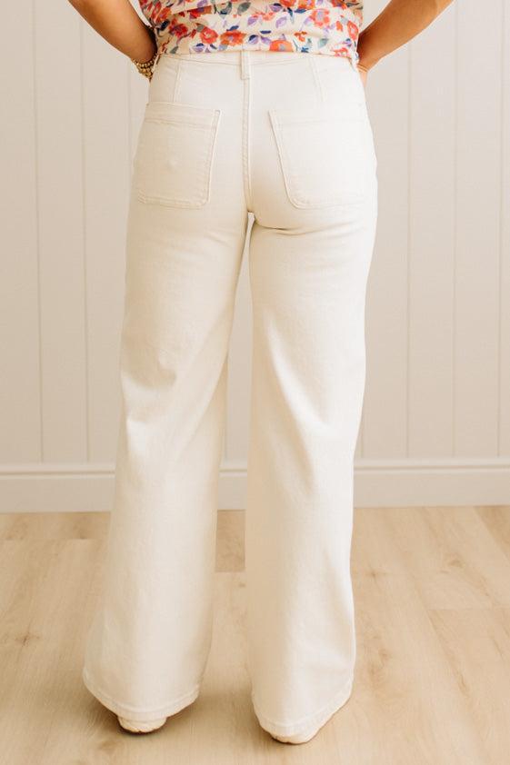 Person wearing white wide-leg pants and a colorful top against a light wooden panel background