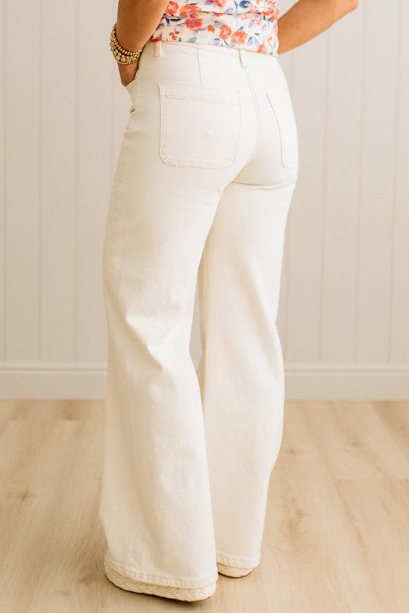 White wide-leg jeans worn by a person on a light wooden floor.