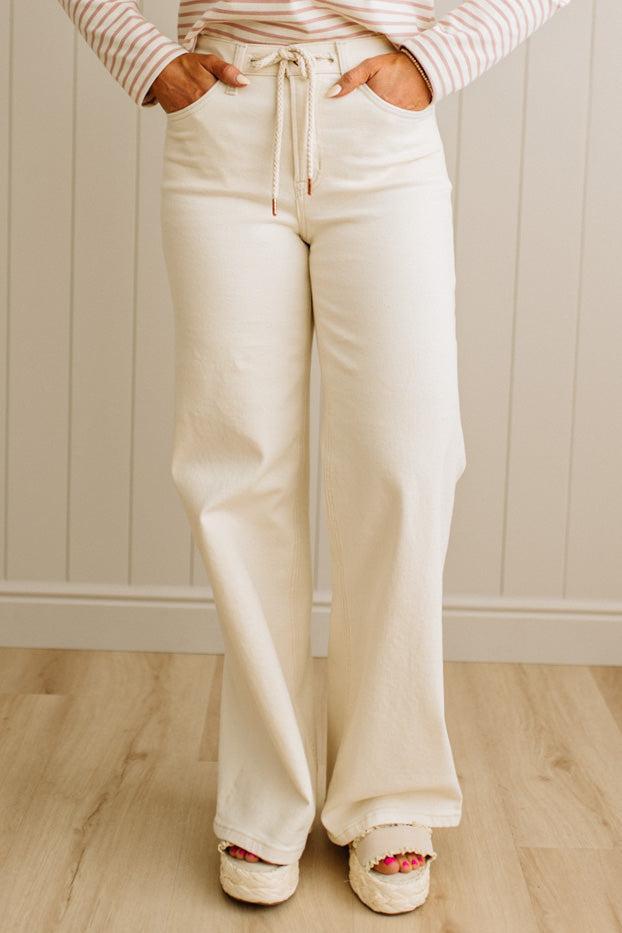 Person wearing white wide-leg pants and a striped shirt against a neutral background