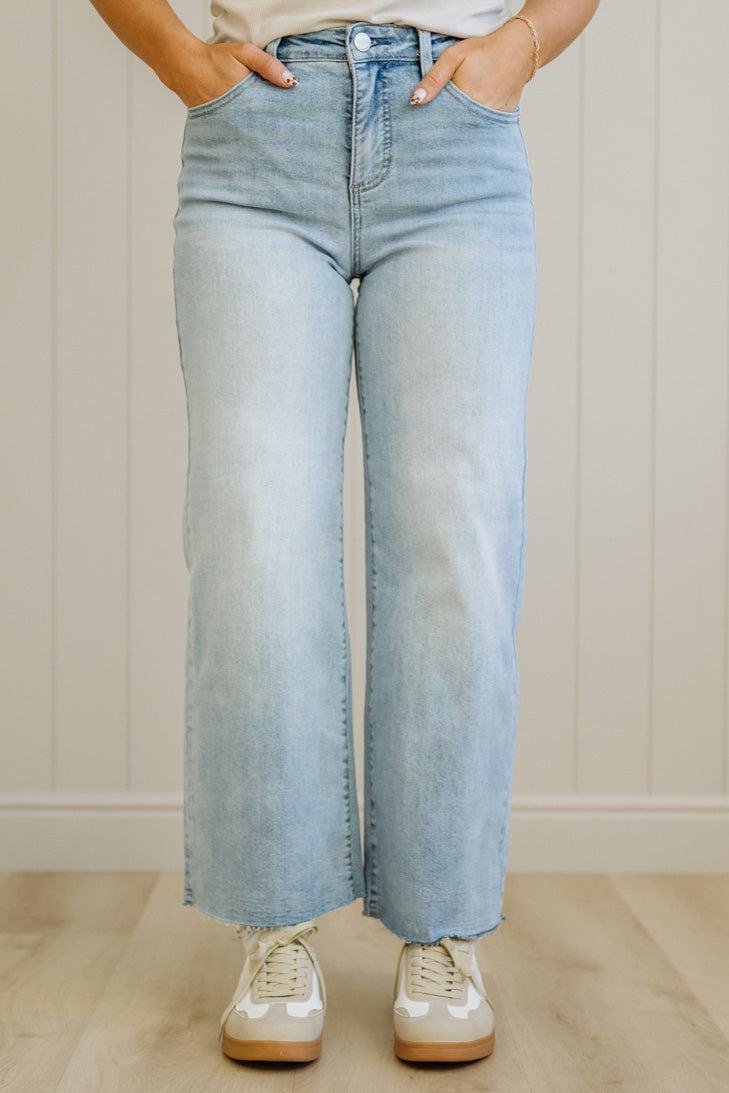 Person wearing light blue jeans and white sneakers against a neutral background