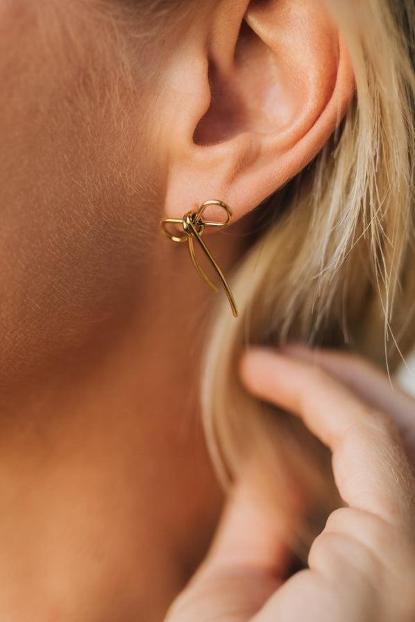Close-up of a person wearing a gold bow-shaped earring.