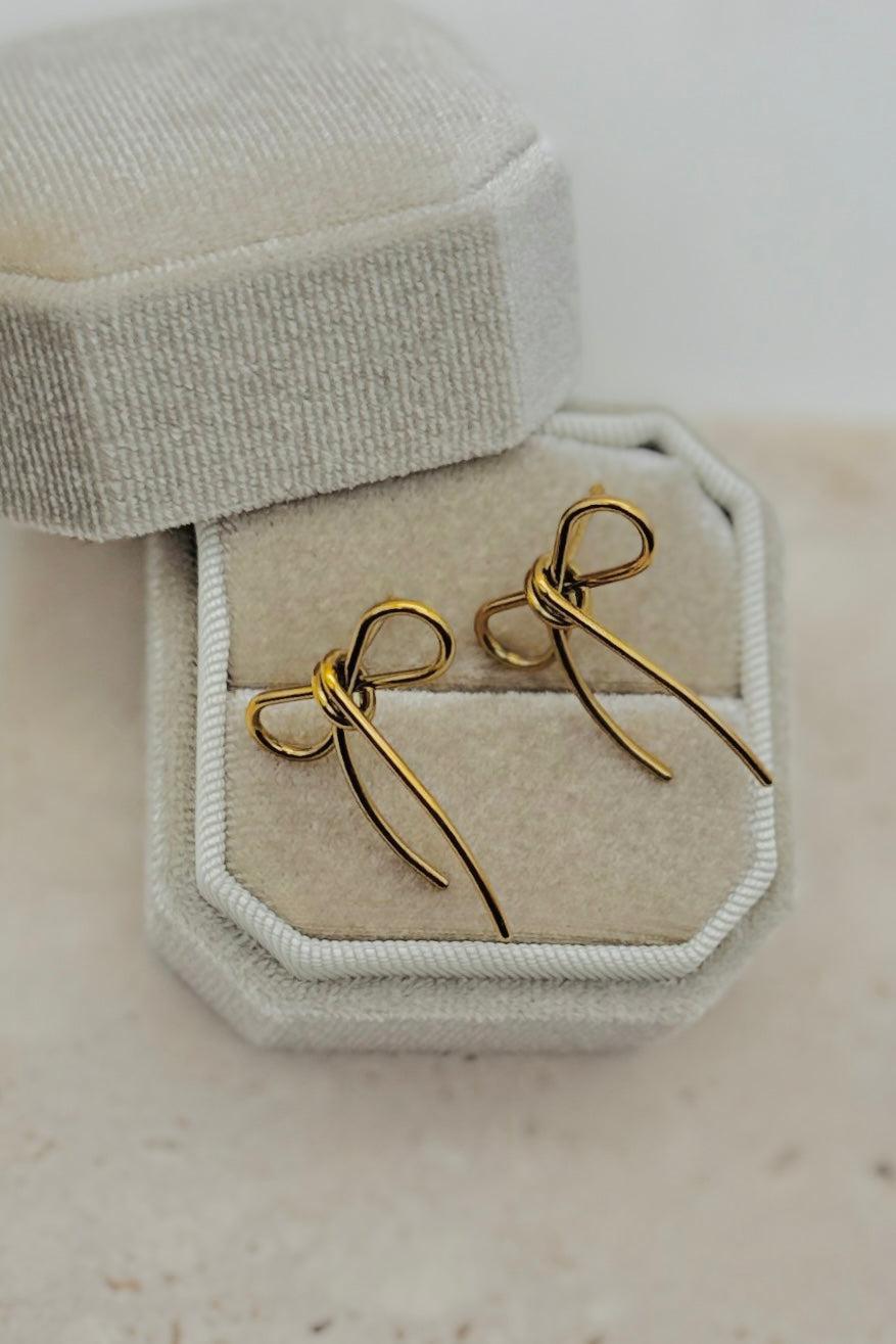 Gold earrings in a hexagonal jewelry box on a light beige background