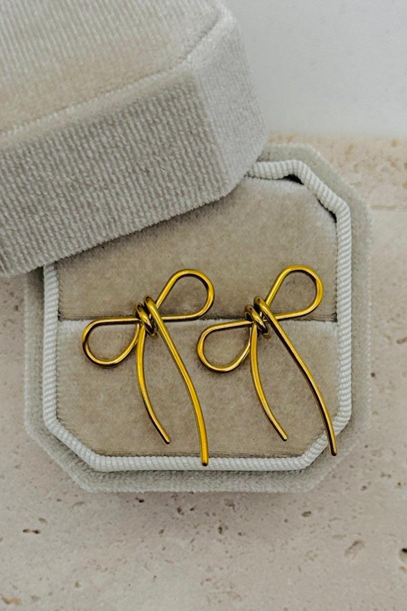 Gold bow-shaped earrings on a textured surface with a neutral background
