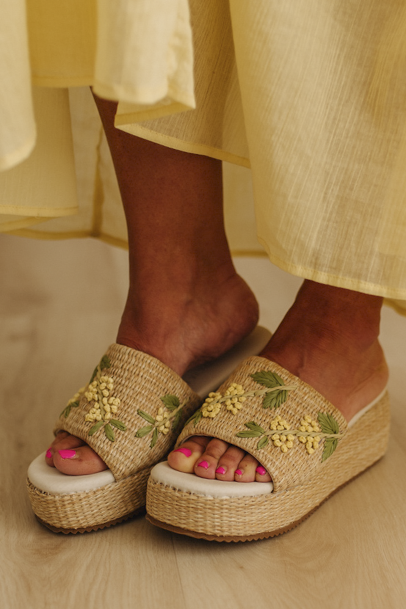 Woman wearing woven raffia base platforms that are detailed with floral embroidery.