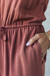 Women wearing a rust colored wide leg jumpsuit with tie waist and pockets.