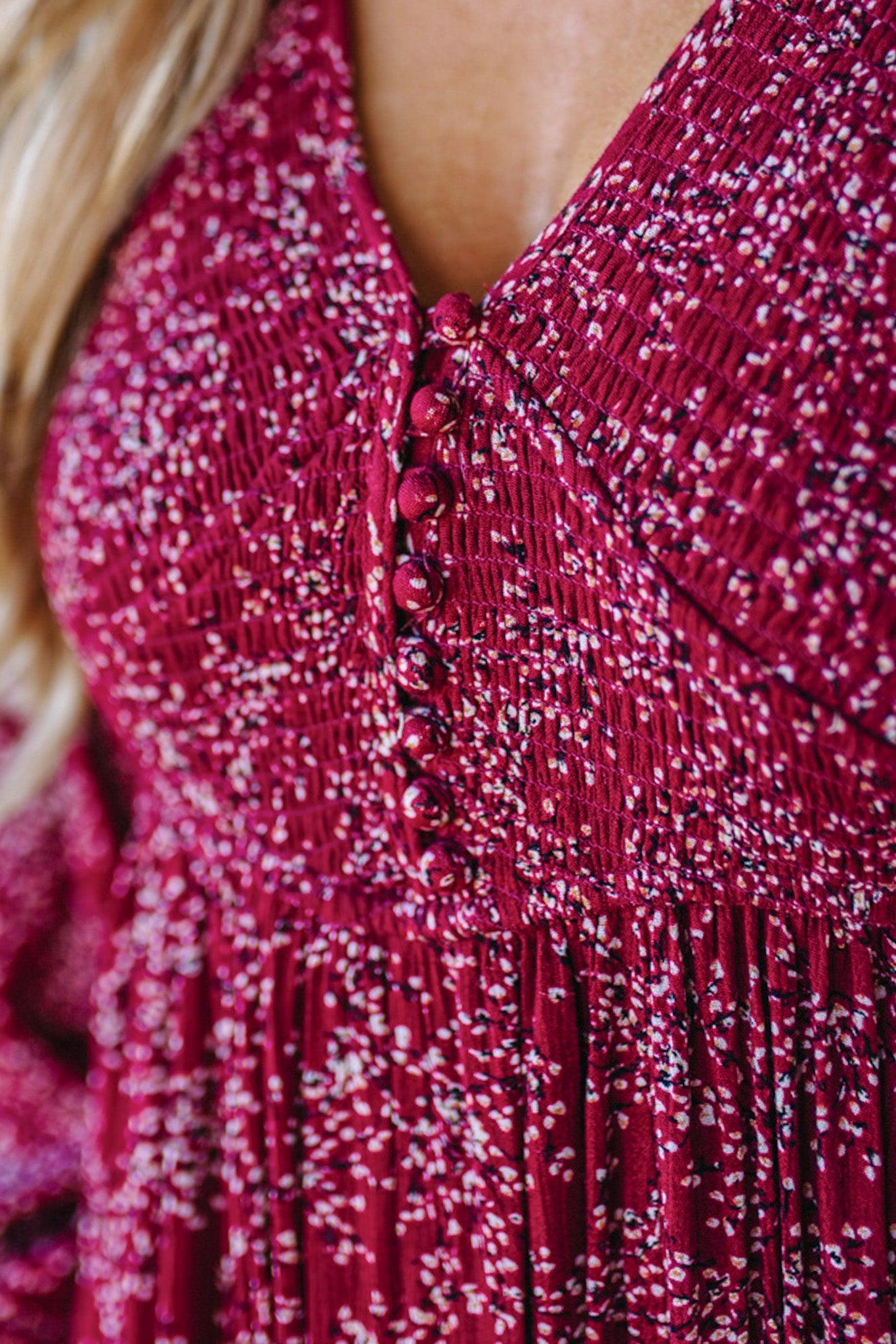 Blonde Woman Wearing a Smocked Floral Maxi Dress with Button Front and v-neckline in a deep wine red color.
