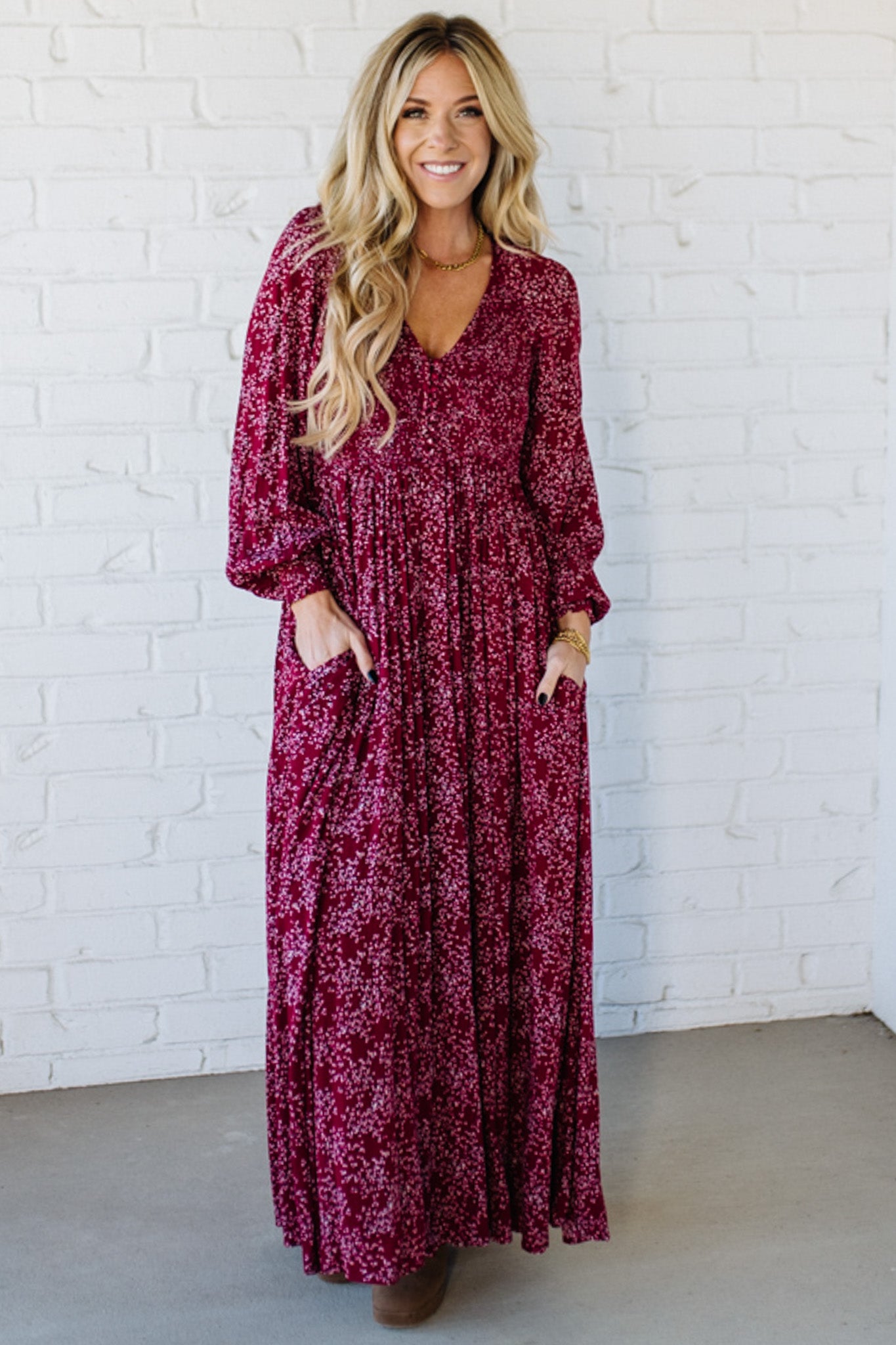 Blonde Woman Wearing a Smocked Floral Maxi Dress with Button Front and v-neckline in a deep wine red color.