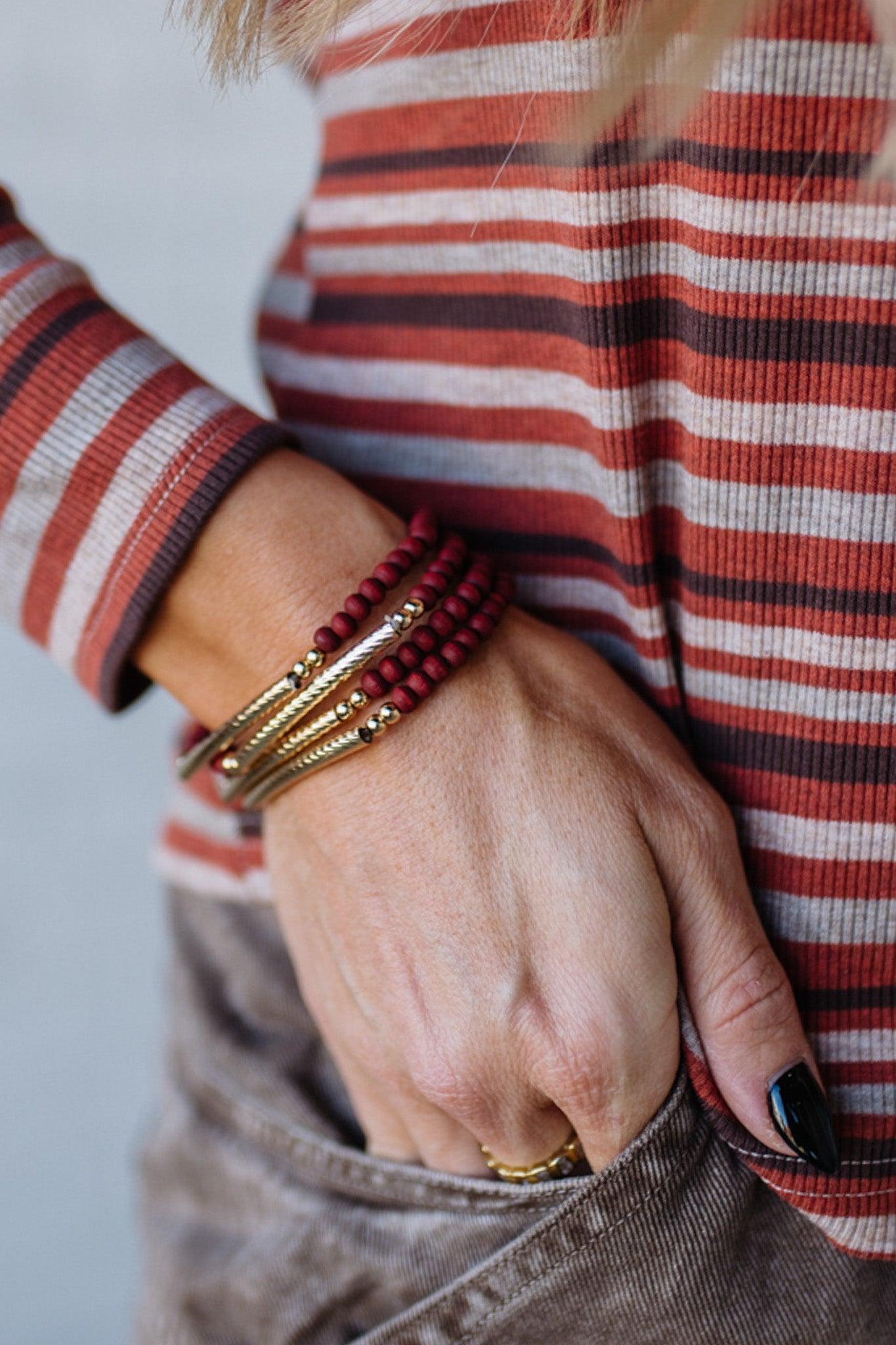 Close-up of a hand wearing multiple bracelets with a striped shirt in the background