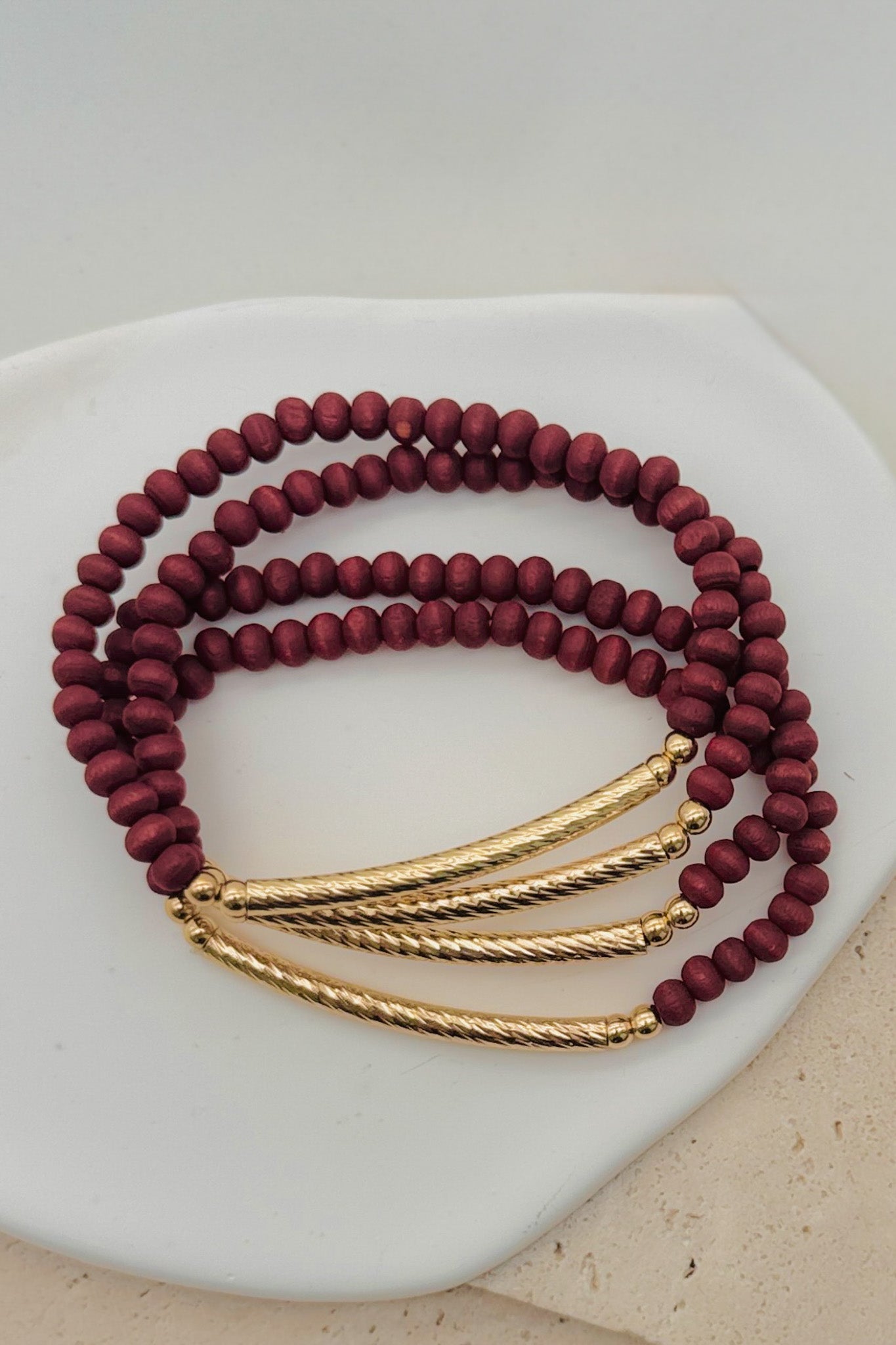 Set of maroon beaded bracelets with gold accents on a white surface