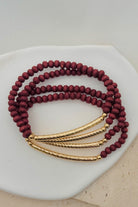 Set of maroon beaded bracelets with gold accents on a white surface