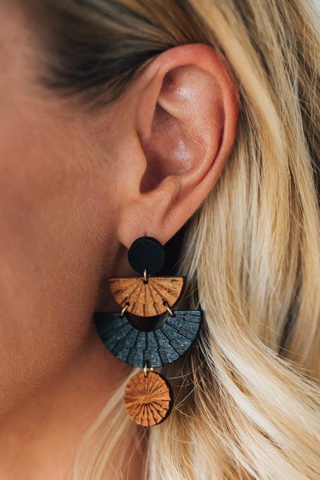 Close-up of an ear wearing a unique earring with wooden and stone-like elements.