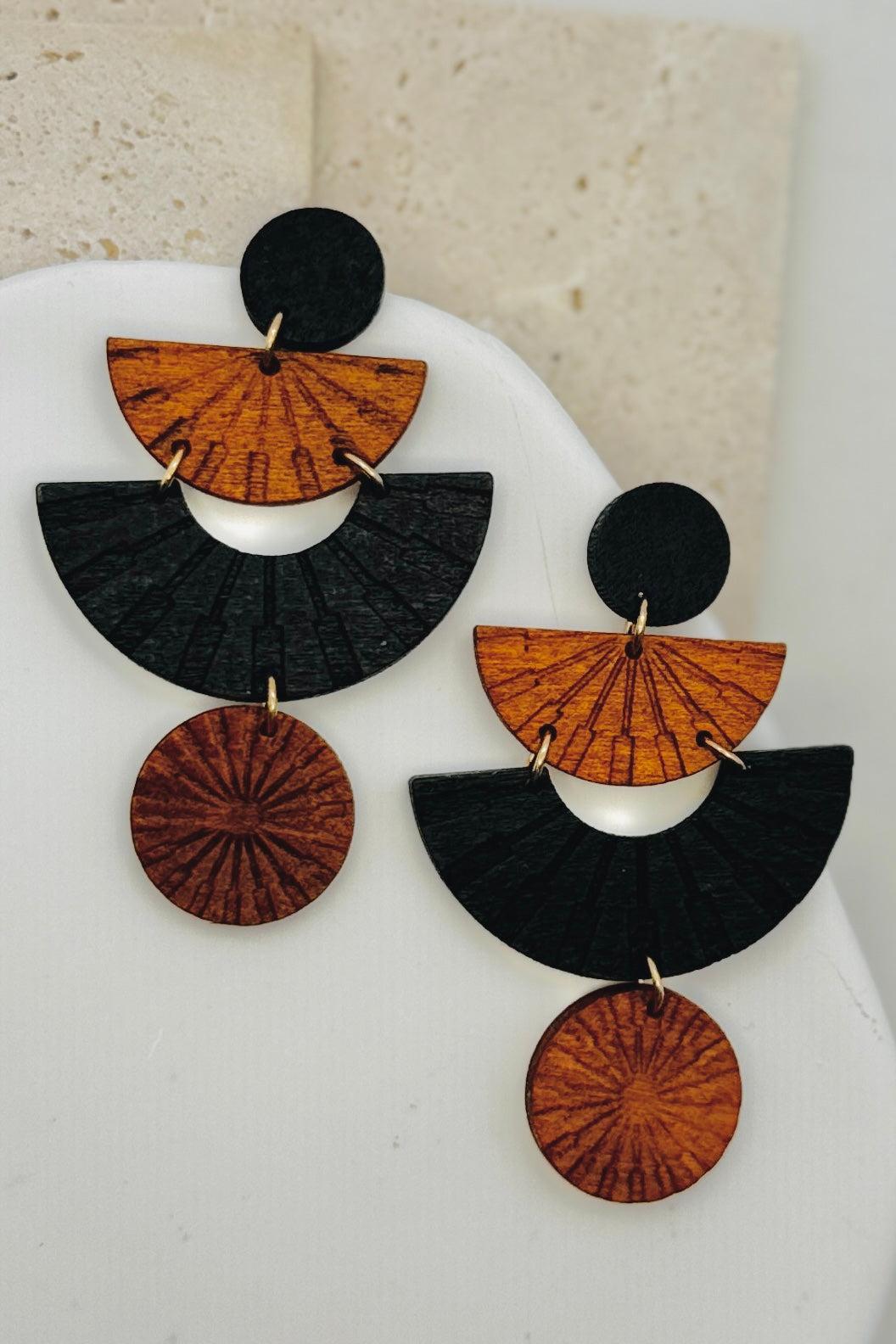 Pair of wooden geometric shapped black and brown earrings on a white stand