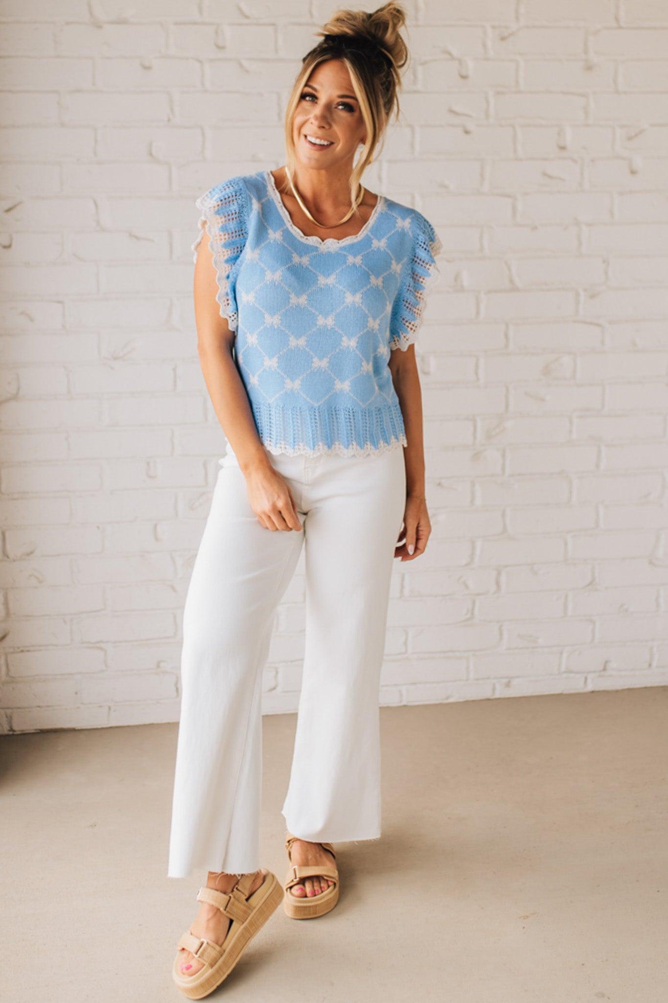 BLONDE WOMAN WEARING A BOW RIBBON PATTERN SWEATER TOP WITH BACK KEY HOLE AND TIE.