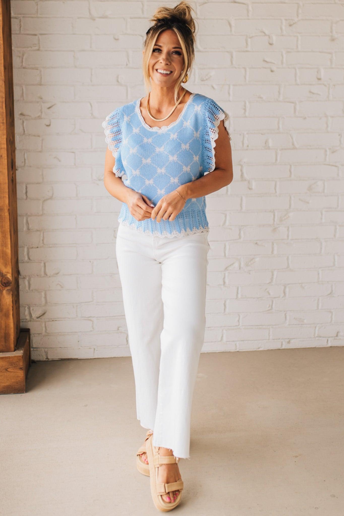 BLONDE WOMAN WEARING A BOW RIBBON PATTERN SWEATER TOP WITH BACK KEY HOLE AND TIE.