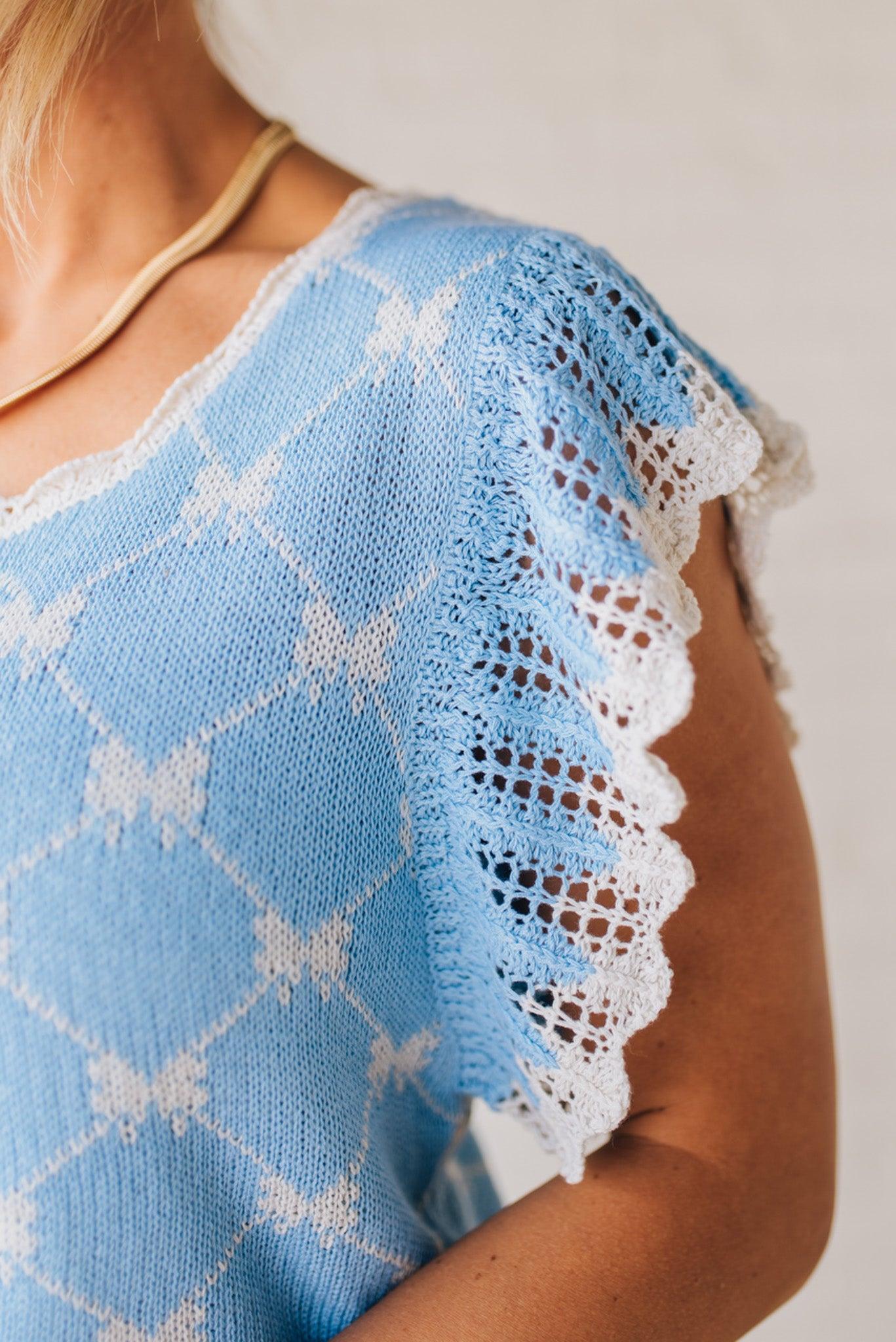 BLONDE WOMAN WEARING A BOW RIBBON PATTERN SWEATER TOP WITH BACK KEY HOLE AND TIE.