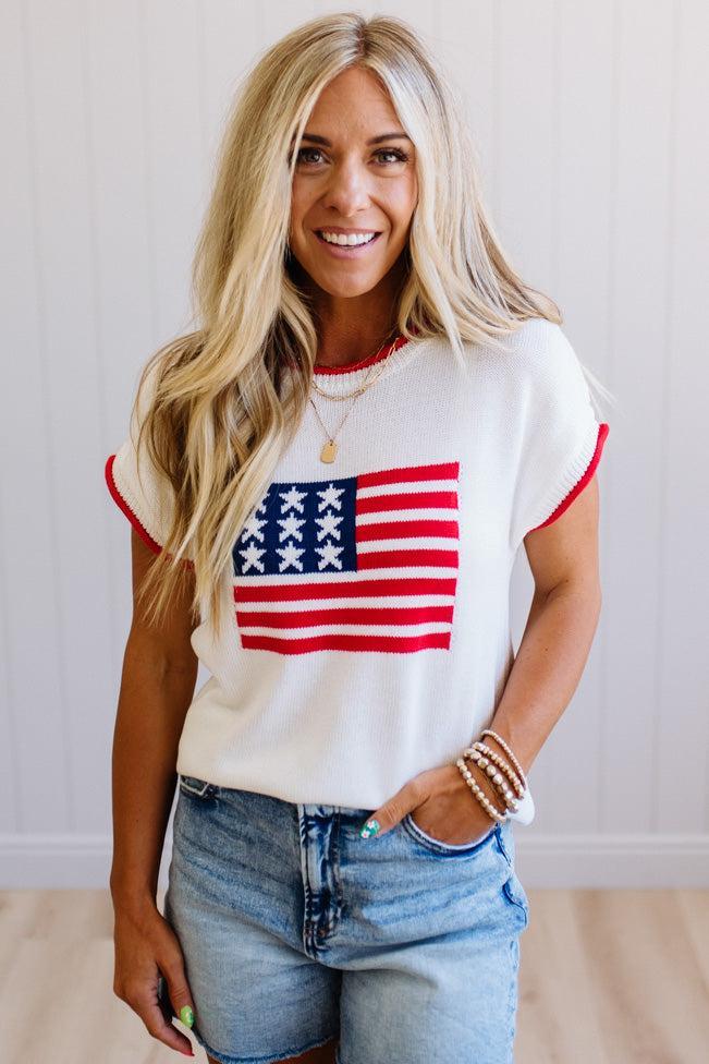 Woman wearing a white t-shirt with an American flag design and denim shorts.