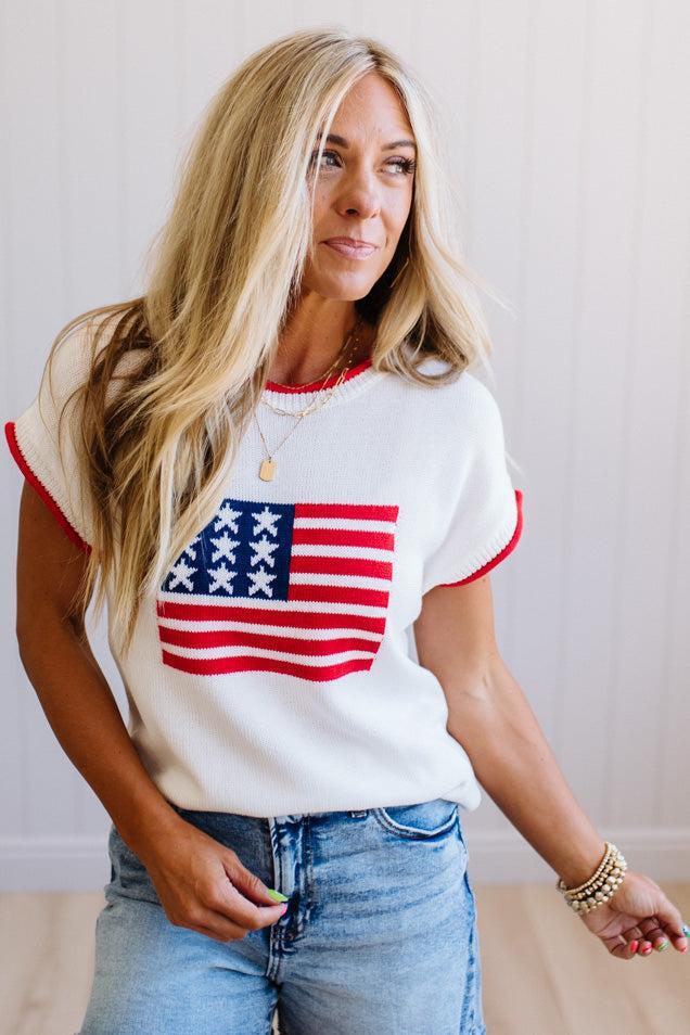 Woman wearing a white t-shirt with an American flag design and blue jeans.