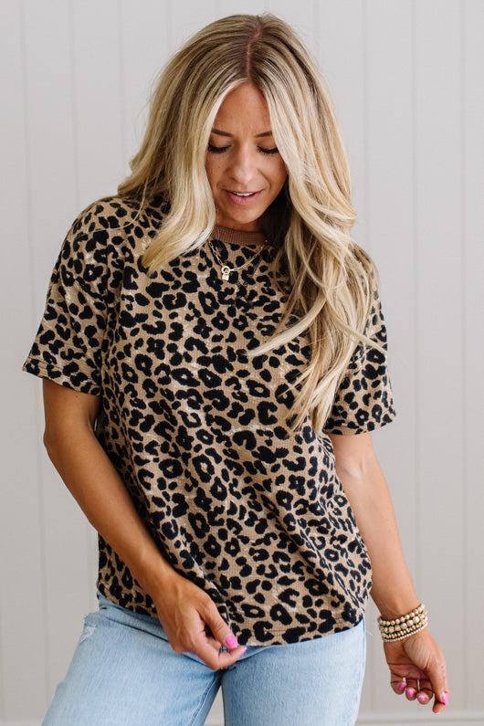 Woman wearing a leopard print shirt and light blue jeans against a plain background