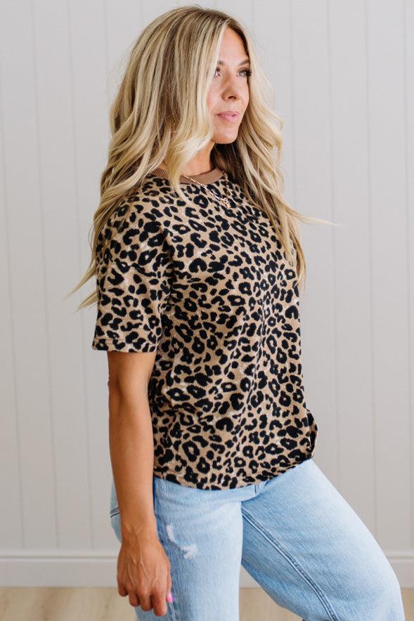 Woman wearing a leopard print top and light blue jeans against a neutral background