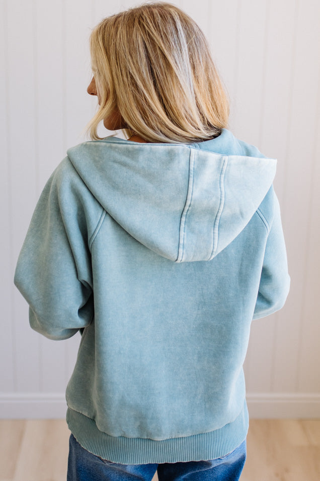 Person wearing a light blue hoodie from behind with a plain background