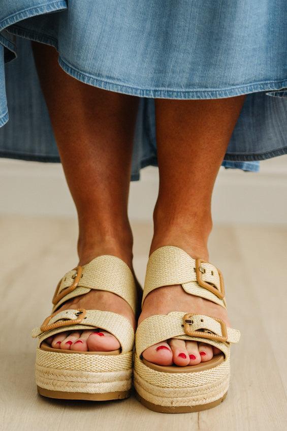 Beige sandals with espadrille sole worn with a blue skirt on a light wooden floor.