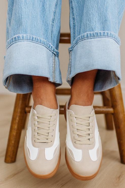 Beige sneakers with white accents worn with rolled-up jeans on a wooden stool.