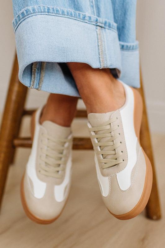 Beige sneakers with brown soles worn with light blue jeans on a wooden floor.