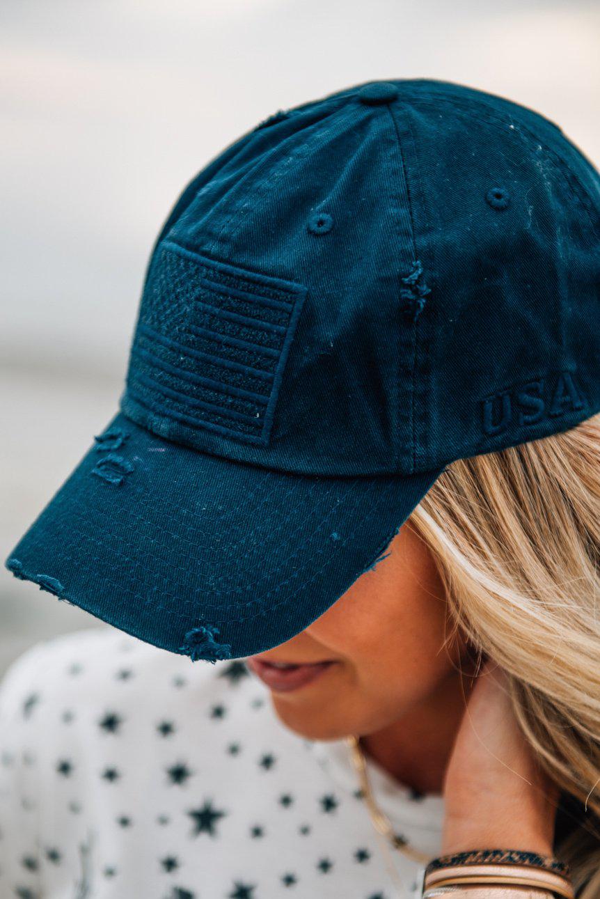Blonde woman wearing a single color distressed american flag hat.