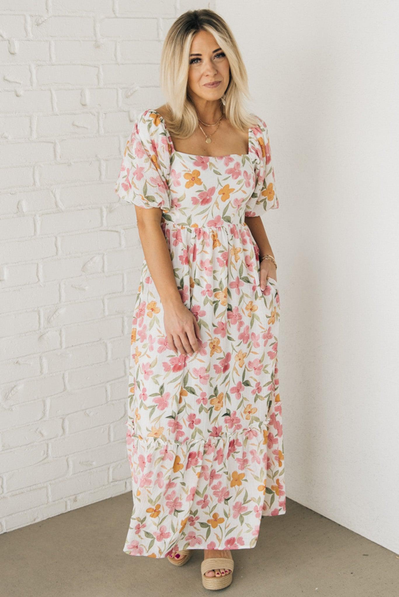 Blonde woman wearing a floral print maxi dress with square neckline and puffed half length sleeves.