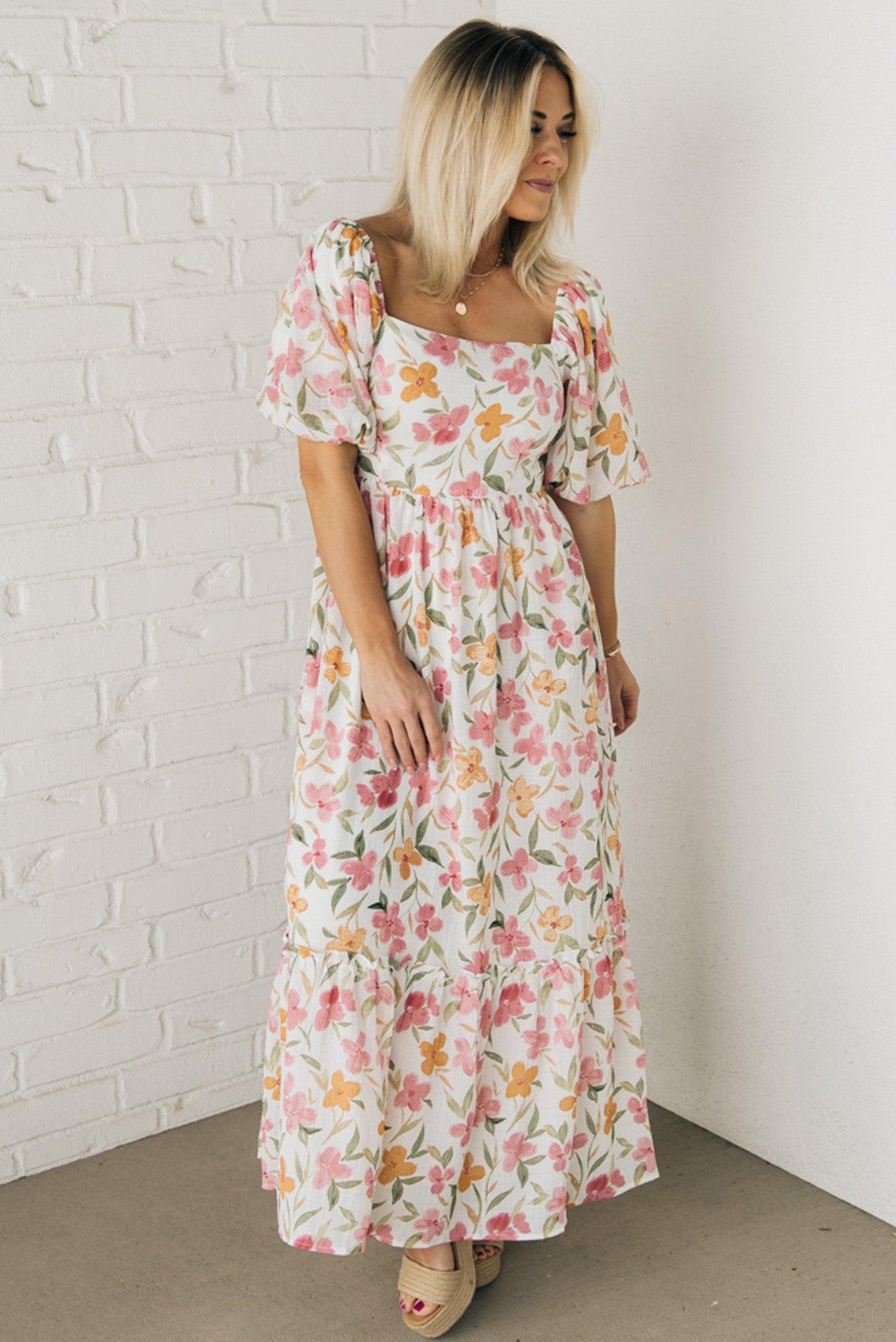 Blonde woman wearing a floral print maxi dress with square neckline and puffed half length sleeves.